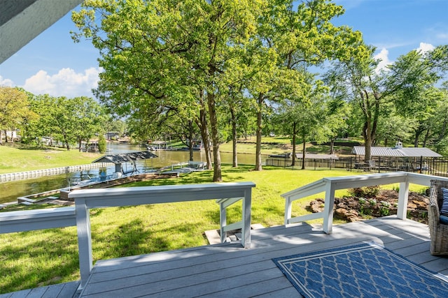 wooden terrace with a water view, fence, and a lawn