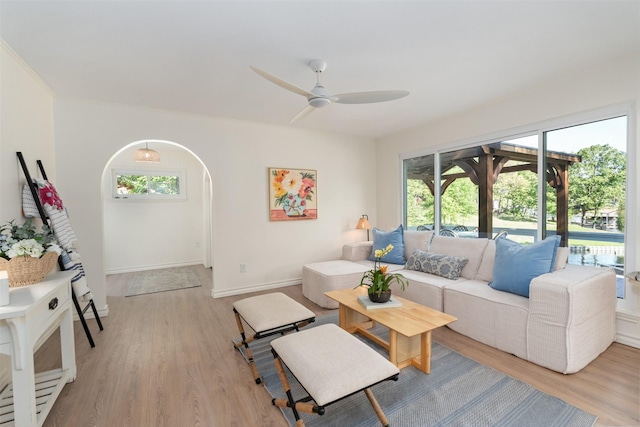 living room featuring baseboards, a ceiling fan, arched walkways, and light wood-style floors
