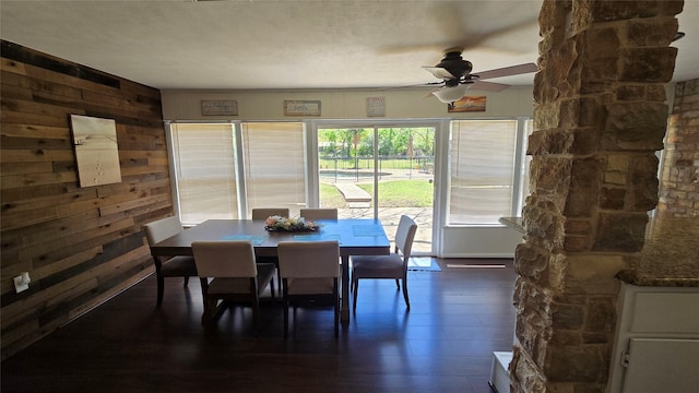 dining room featuring wood walls, dark wood-type flooring, and ceiling fan