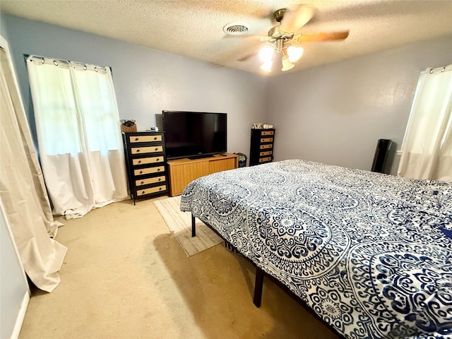 bedroom with visible vents, a ceiling fan, light carpet, and a textured ceiling