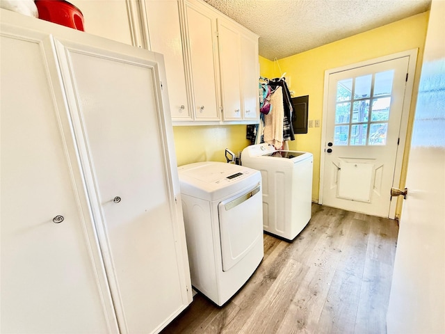 laundry area with a textured ceiling, washer and dryer, cabinet space, and light wood-style floors