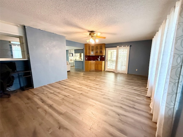 unfurnished living room featuring ceiling fan, a textured ceiling, and light wood-style flooring