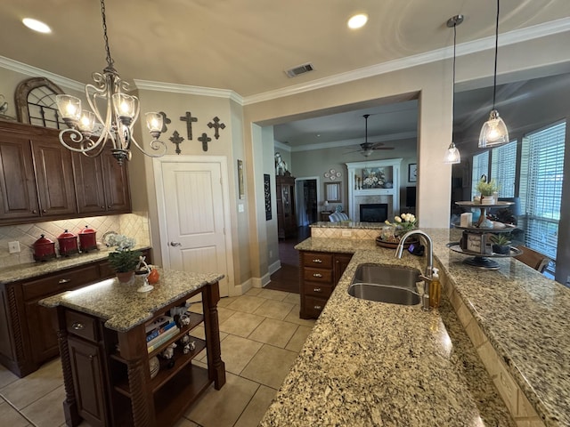 kitchen featuring crown molding, ceiling fan with notable chandelier, light stone countertops, a sink, and backsplash