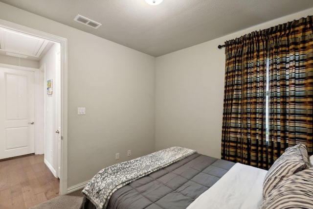 bedroom featuring baseboards, attic access, wood finished floors, and visible vents