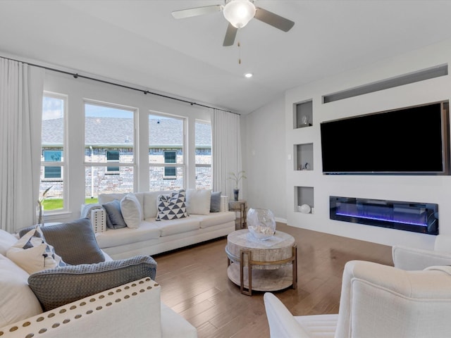living room with a ceiling fan, vaulted ceiling, built in shelves, wood finished floors, and a glass covered fireplace