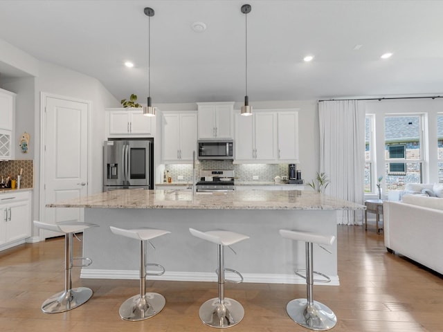 kitchen featuring appliances with stainless steel finishes, light wood finished floors, a breakfast bar area, white cabinetry, and tasteful backsplash
