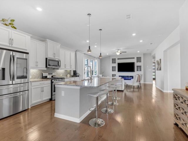 kitchen featuring light stone countertops, stainless steel appliances, a ceiling fan, open floor plan, and white cabinetry