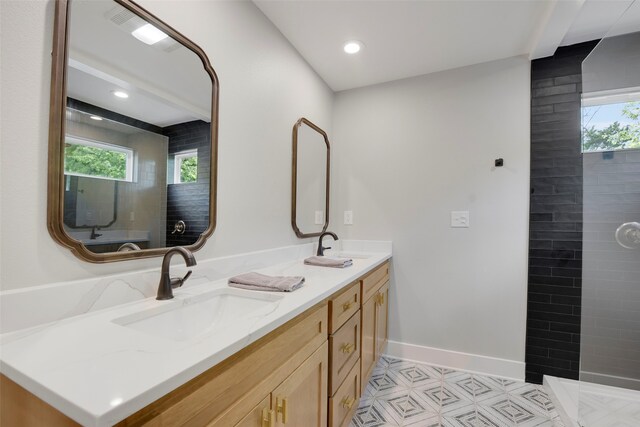 bathroom with baseboards, a sink, double vanity, and tiled shower