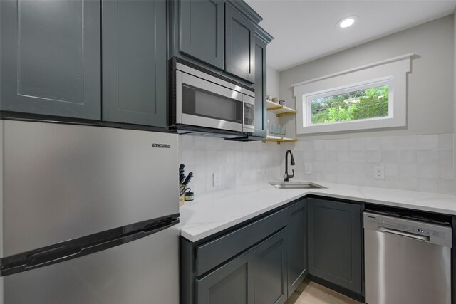 kitchen with decorative backsplash, light stone countertops, stainless steel appliances, and a sink