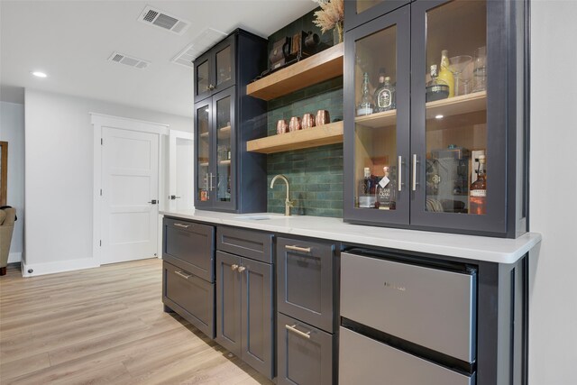 bar featuring a sink, fridge, light wood-type flooring, wet bar, and visible vents
