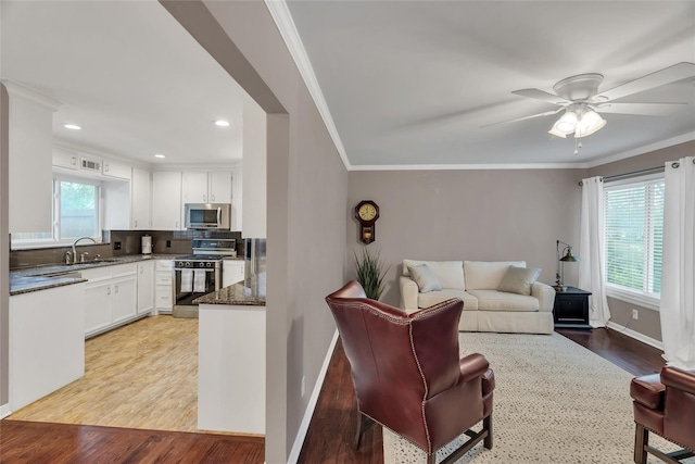 living room featuring crown molding, baseboards, a ceiling fan, and light wood-style floors