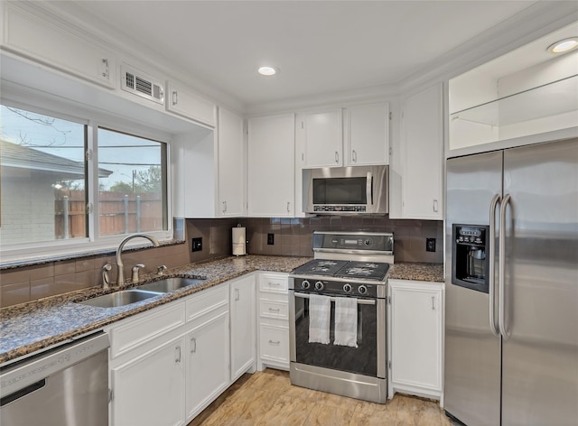 kitchen featuring dark stone counters, appliances with stainless steel finishes, a sink, and white cabinetry