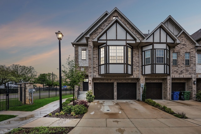 tudor home with stucco siding, fence, brick siding, a garage, and concrete driveway