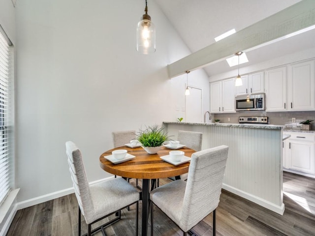 dining room with dark wood-type flooring, baseboards, and lofted ceiling with skylight