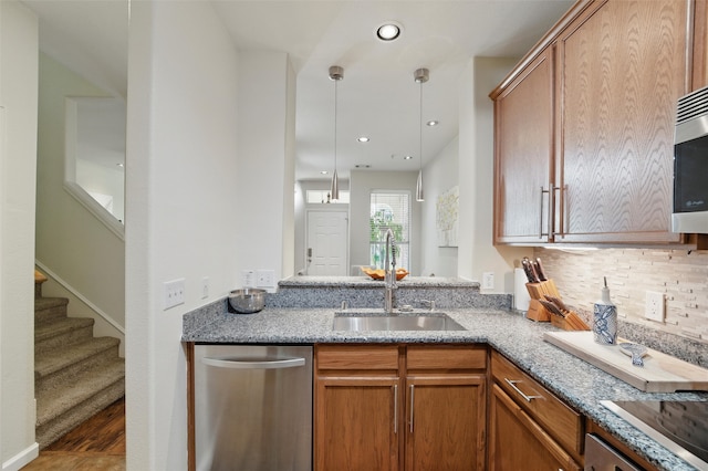 kitchen with brown cabinets, a sink, light stone counters, stainless steel dishwasher, and wood finished floors