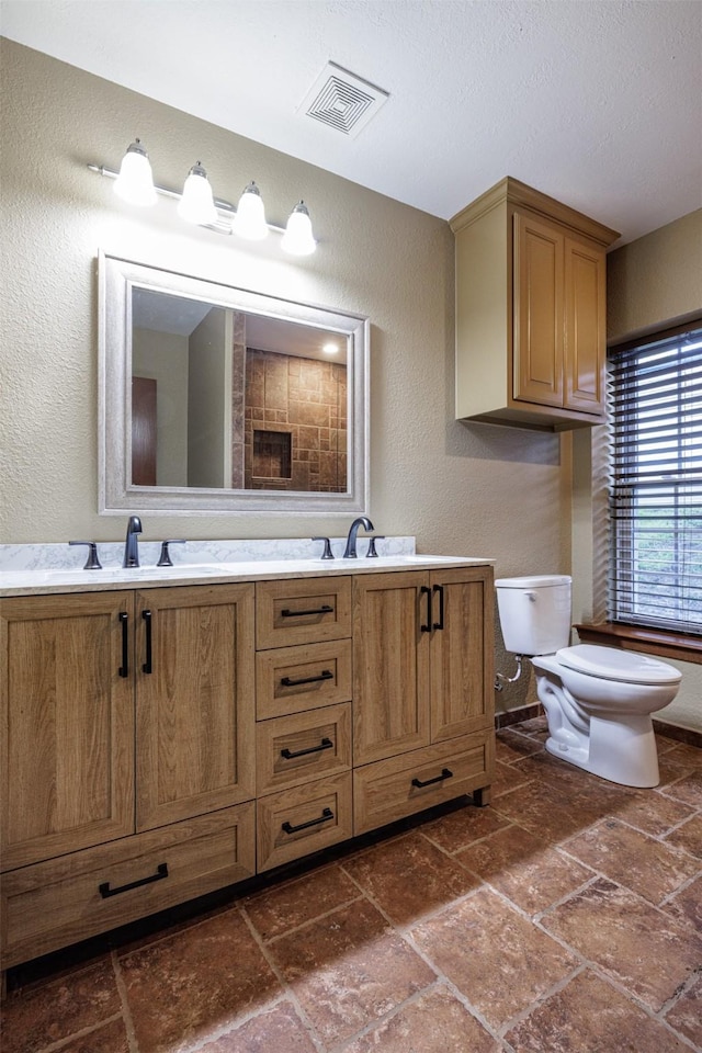 bathroom with a textured wall, visible vents, toilet, a sink, and stone tile flooring