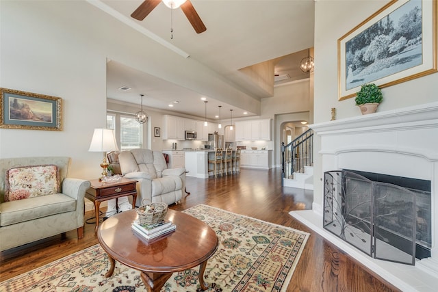 781 Bosley Dr, Fate, TX 75087 - living area with crown molding, dark wood-type flooring, ceiling fan, stairs, and a fireplace with raised hearth