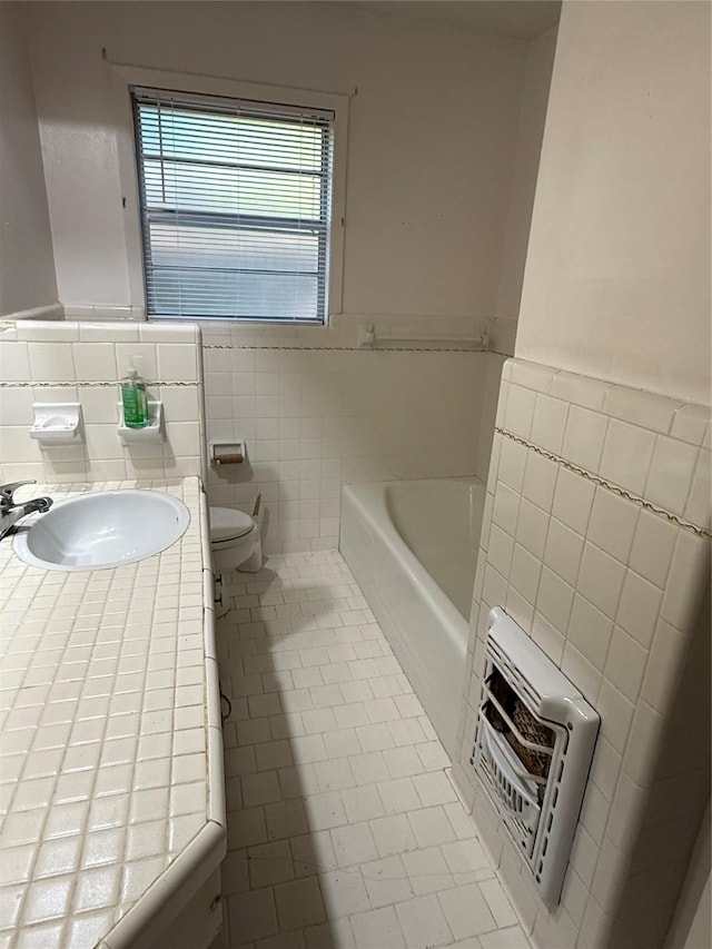 full bath with toilet, a wainscoted wall, heating unit, a bath, and tile walls
