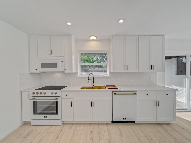 kitchen featuring a sink, white cabinetry, white appliances, and light wood-style floors