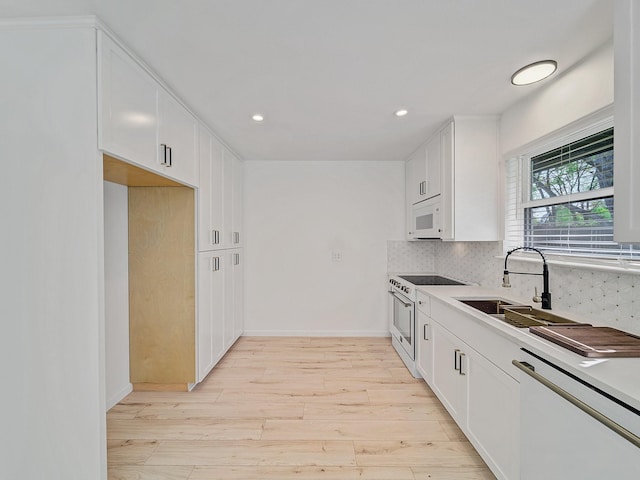 kitchen featuring white appliances, white cabinetry, light wood-style floors, decorative backsplash, and a sink