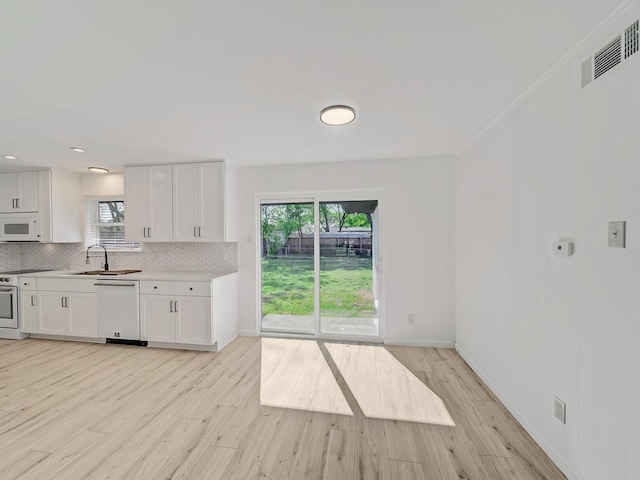 kitchen with a sink, backsplash, light wood-style flooring, and white appliances
