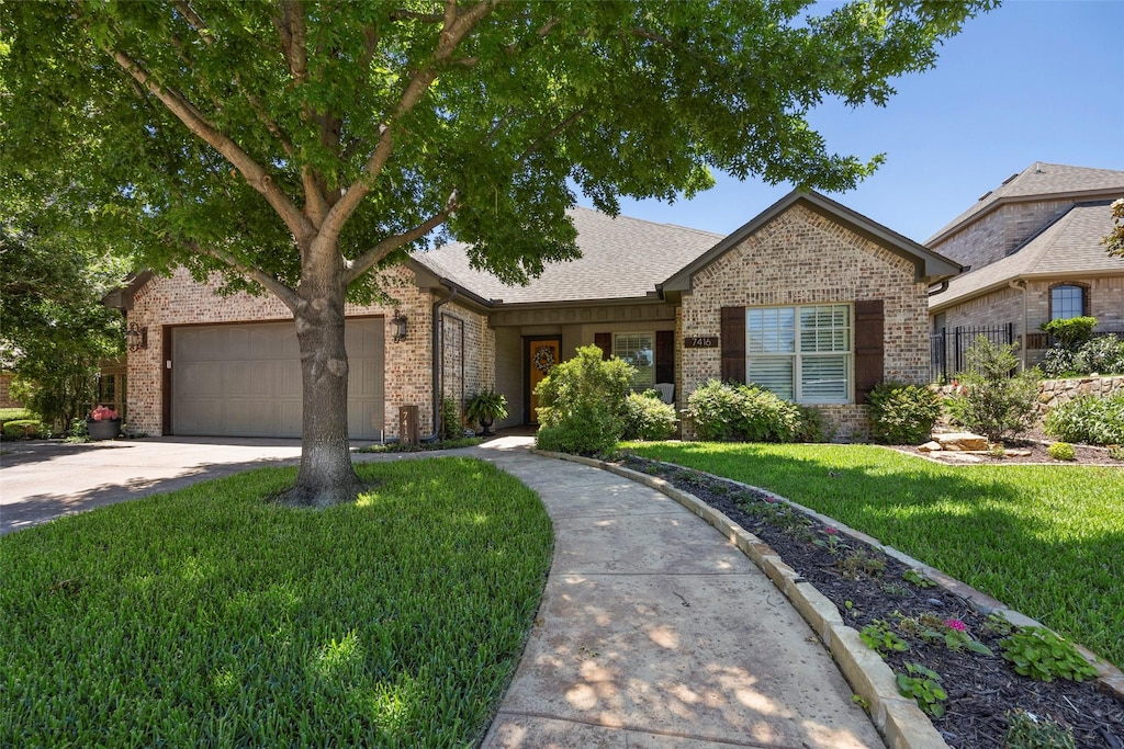 ranch-style house with a front yard, a shingled roof, a garage, concrete driveway, and brick siding