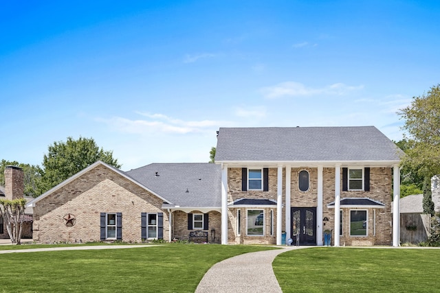 greek revival inspired property with a front yard, brick siding, and a shingled roof