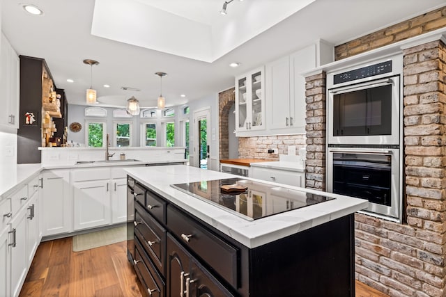 kitchen with light wood-type flooring, stainless steel double oven, a sink, and black electric cooktop