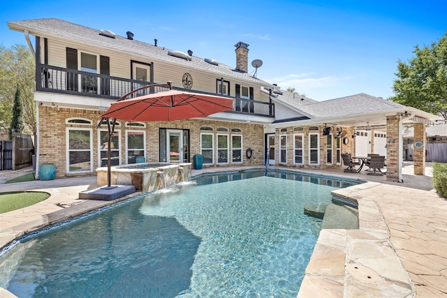 back of house with brick siding, an in ground hot tub, a patio, and a balcony