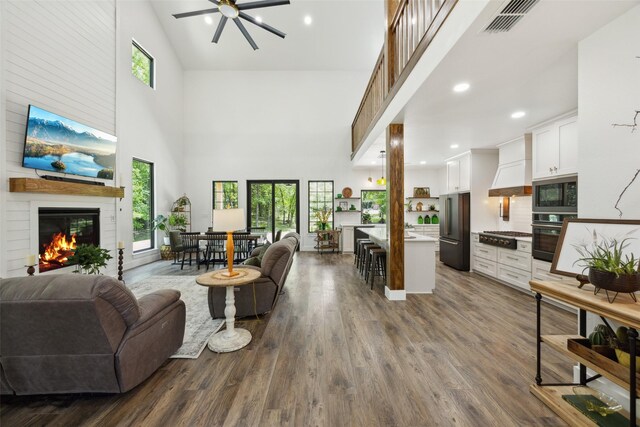 living area featuring a fireplace, dark wood-style floors, visible vents, ceiling fan, and high vaulted ceiling