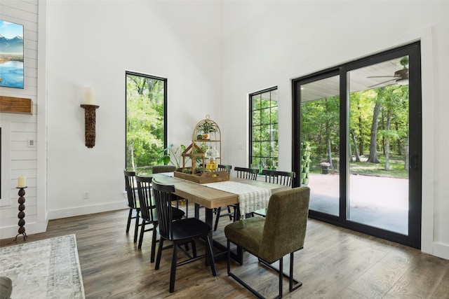 dining space featuring a high ceiling, wood finished floors, baseboards, and a healthy amount of sunlight
