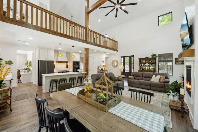dining area featuring a lit fireplace, wood finished floors, high vaulted ceiling, and ceiling fan