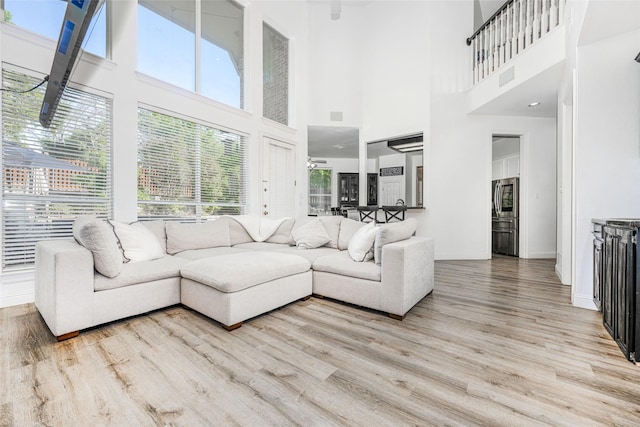 living room with plenty of natural light, light wood-type flooring, visible vents, and a towering ceiling