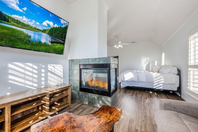 bedroom featuring crown molding, lofted ceiling, wood finished floors, and a tiled fireplace