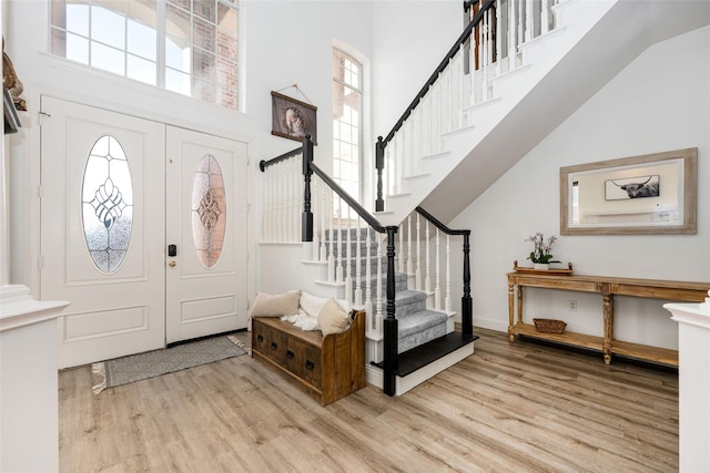 foyer entrance with stairway, a wealth of natural light, wood finished floors, and a towering ceiling