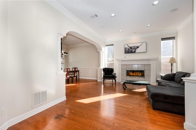 living area featuring arched walkways, decorative columns, a tile fireplace, and visible vents