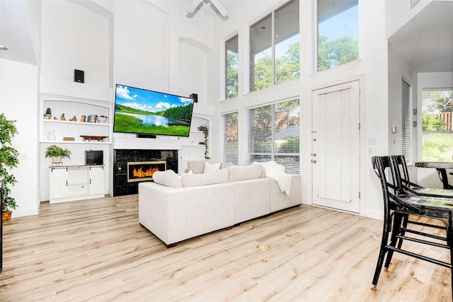 living area with a high end fireplace, a towering ceiling, wood finished floors, and ceiling fan