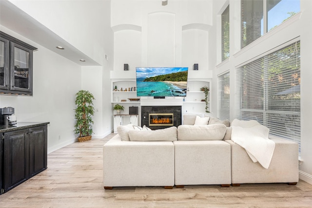 living area featuring a high ceiling, baseboards, a high end fireplace, and light wood-style floors