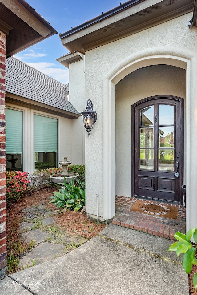 doorway to property with stucco siding and a shingled roof