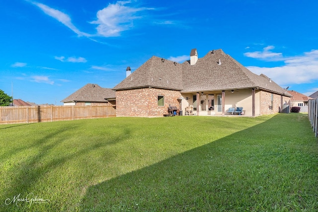 rear view of house featuring brick siding, a fenced backyard, a lawn, and a chimney