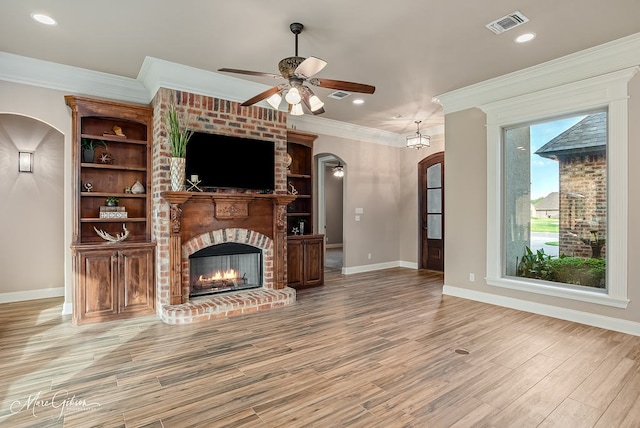 unfurnished living room featuring arched walkways, a ceiling fan, ornamental molding, light wood finished floors, and baseboards