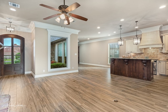 unfurnished living room featuring ornamental molding, visible vents, baseboards, and a wealth of natural light