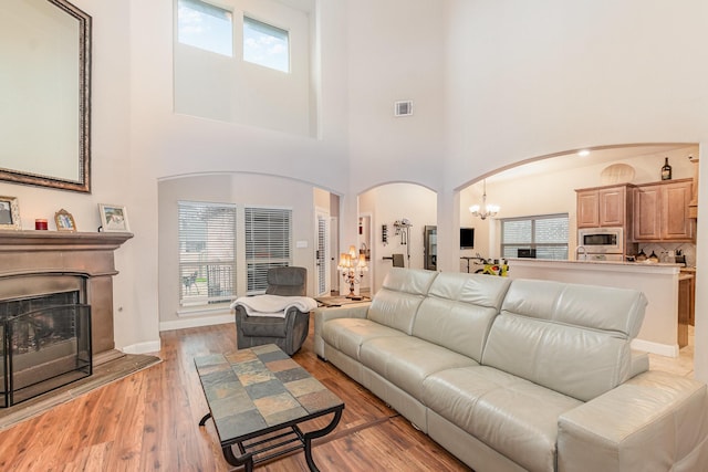 living room with a chandelier, a high ceiling, a fireplace with raised hearth, visible vents, and arched walkways