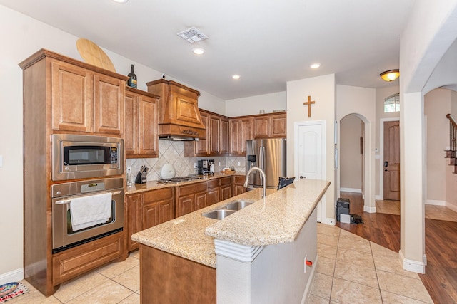 kitchen featuring light stone countertops, visible vents, appliances with stainless steel finishes, arched walkways, and a sink