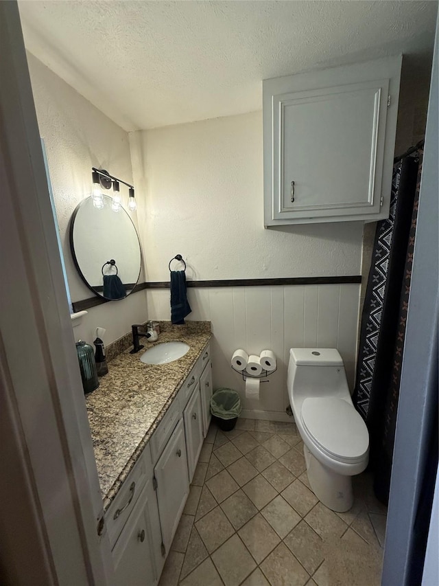 2909 Oakridge Dr, Corsicana, TX 75110 - full bathroom featuring a textured ceiling, vanity, toilet, tile patterned floors, and wainscoting