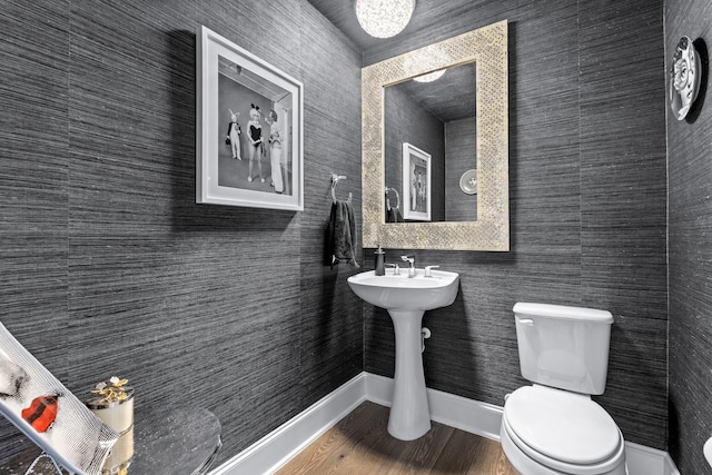 half bath with baseboards, toilet, and wood finished floors