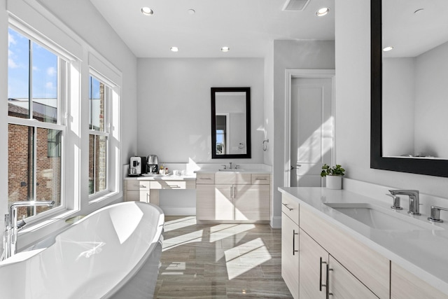 bathroom featuring a freestanding bath, two vanities, a sink, and recessed lighting