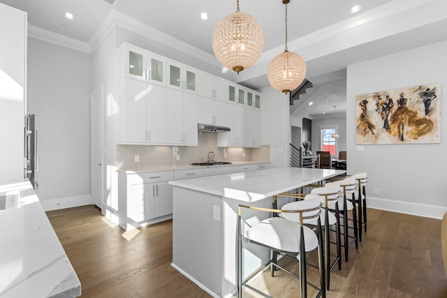 kitchen featuring dark wood-style flooring, an inviting chandelier, ornamental molding, recessed lighting, and under cabinet range hood