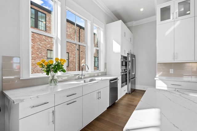 kitchen with light stone counters, crown molding, dark wood-type flooring, appliances with stainless steel finishes, and a sink