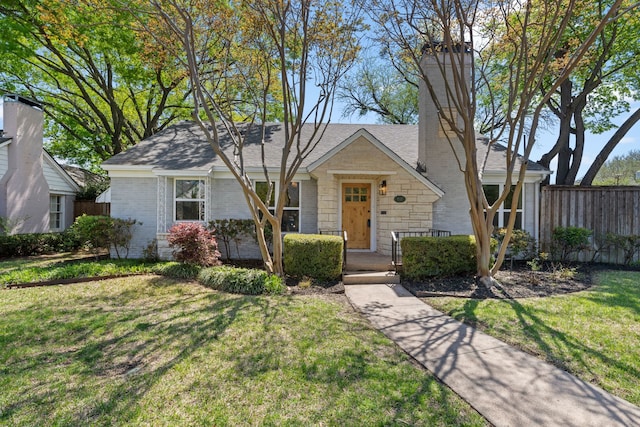 view of front facade with a front yard, a shingled roof, stone siding, a chimney, and fence